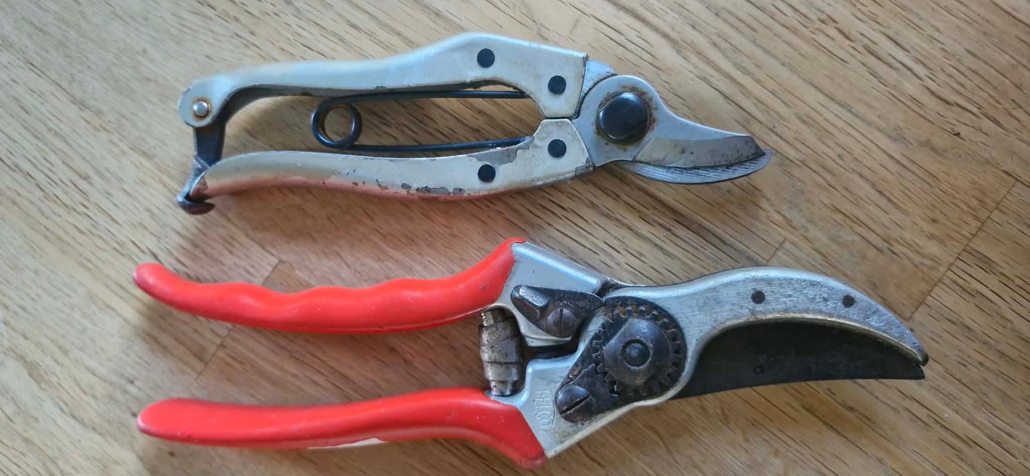 Två sekatörer av olika modeller liggande på ett trägolv