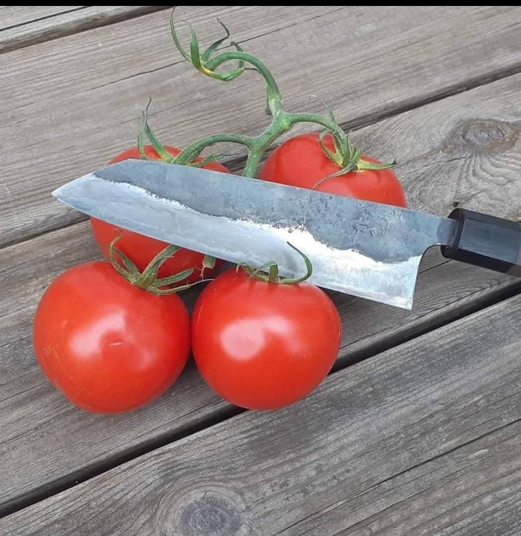 En nyslipad kniv vilar mot mogna tomater på ett träbord