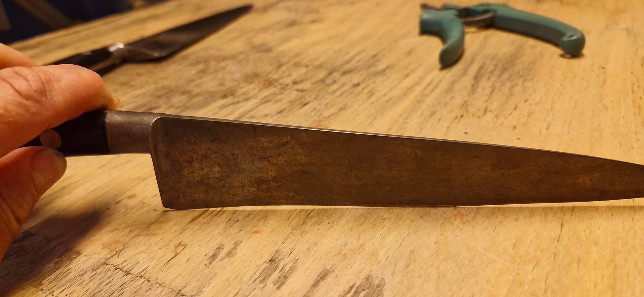 Hand som håller en kniv, med en sekatör synlig i bakgrunden